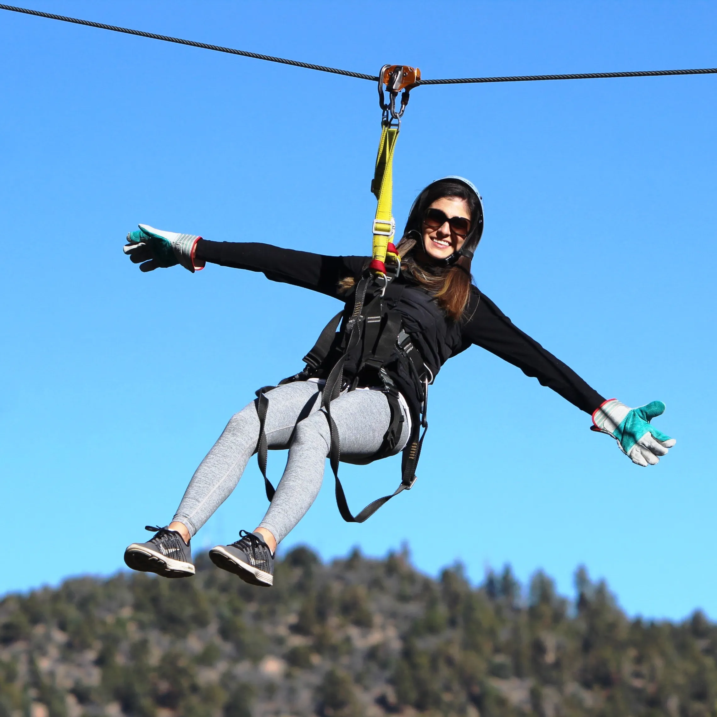 Woman with arms out on zipline in front of blue sky