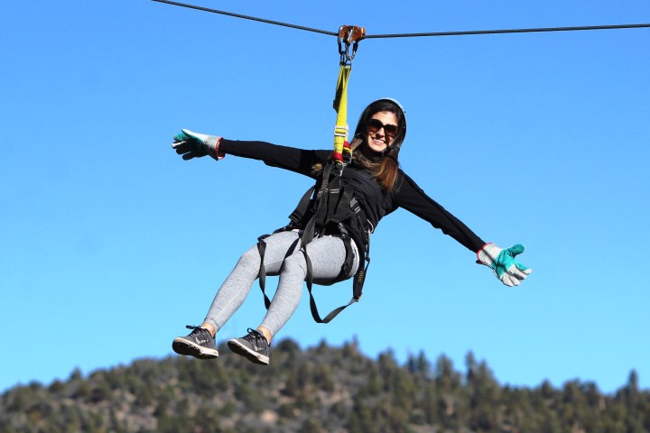 Woman with arms out on zipline in front of blue sky